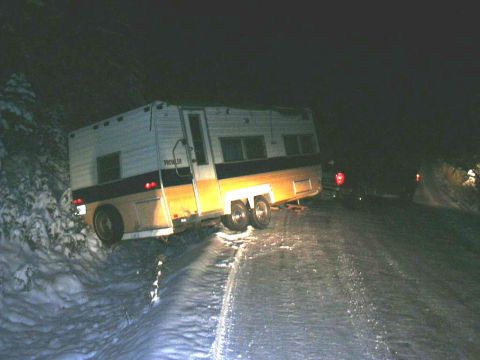 1991 Ford Bronco - A camper trailer is stuck on a snowy road at night, with another vehicle's taillight visible in the distance.