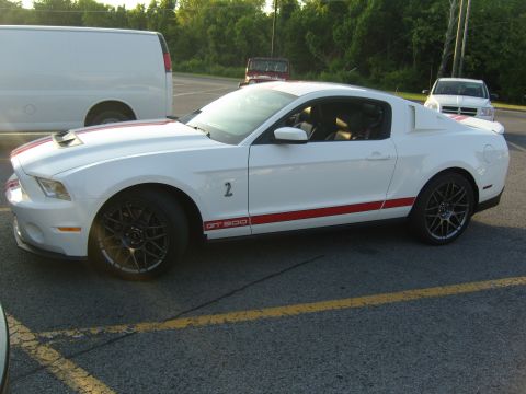 2007 Ford Mustang - A white 2007 Ford Mustang GT500 with red racing stripes and custom black wheels is parked in a lot.