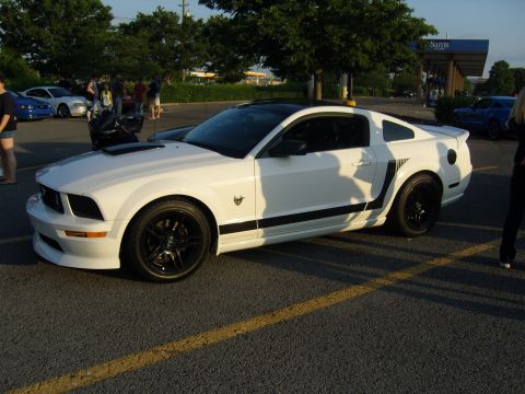 2007 Ford Mustang - A white Ford Mustang with black racing stripes is parked in a lot, with other vehicles and people visible in the background.