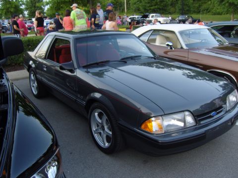 2007 Ford Mustang - A dark gray Ford Mustang is parked at a car show, with other vehicles and people in the background.