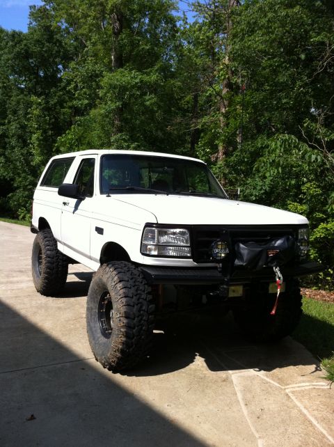 1996 Ford Bronco - Three-quarter front view of a clean lifted white full-size Ford Bronco on a concrete driveway, fitted with a black winch bumper wearing a W…