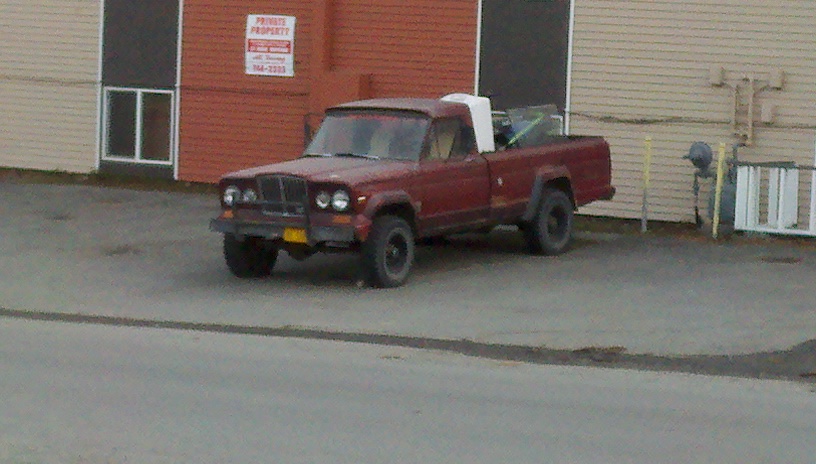 Red pickup truck with a white cap on the bed, parked outside a building