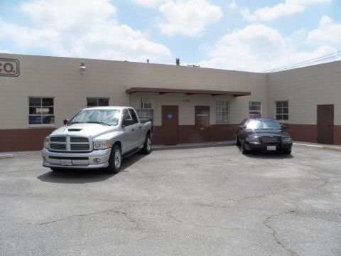 2003 Ford Crown Victoria - Silver Ram with hood scoop and black Crown Victoria flank an entrance under a beige warehouse facade