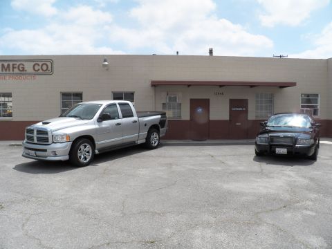 2003 Ford Crown Victoria - Silver Dodge Ram with hood scoop next to a dark sedan, building signage reads MFG CO Products