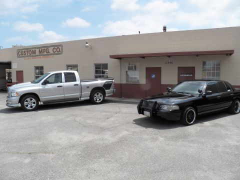 2003 Ford Crown Victoria - Silver Ram pickup and black Crown Victoria with push bar parked by Custom Mfg Co warehouse front