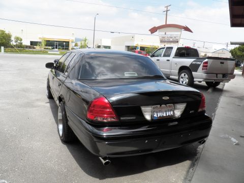 2003 Ford Crown Victoria - Tail of a black Ford sedan showing the EVILVIC plate, Ford trunk badge and twin exhaust outlets.