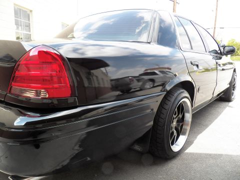 2003 Ford Crown Victoria - Close rear three-quarter of a glossy black sedan showing taillight, fender and a black multi-spoke wheel.