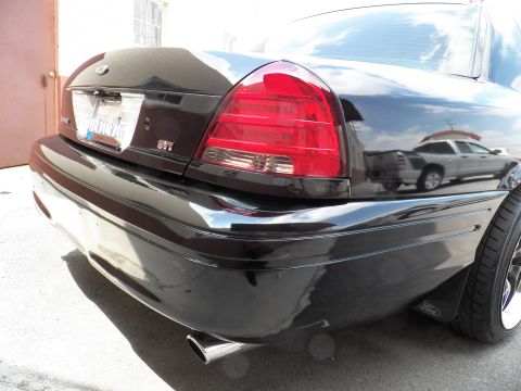 2003 Ford Crown Victoria - Black sedan rear detail with SVT badge, taillight and a chrome exhaust outlet, reflecting a nearby SUV.