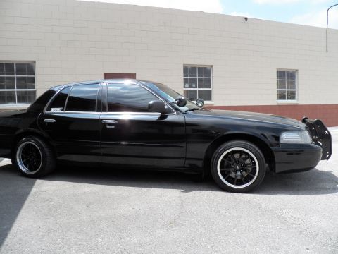 2003 Ford Crown Victoria - Black full-size sedan in profile with chrome window trim, front push bar and black multi-spoke wheels.