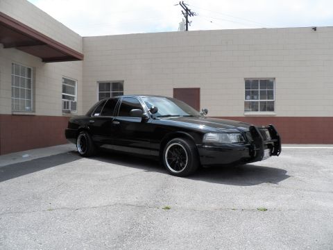 2003 Ford Crown Victoria - Lowered black sedan with a front grille guard and pillar spotlight parked at an industrial building.