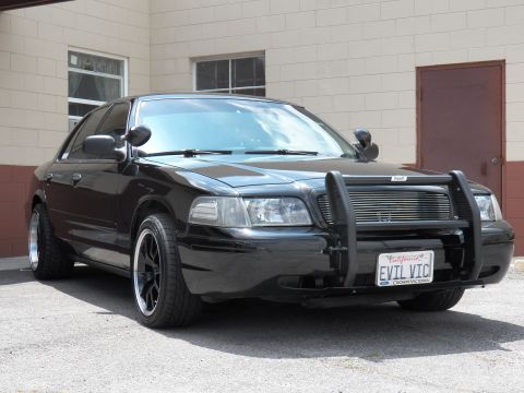 2003 Ford Crown Victoria - Black sedan front-right view with grille guard, spotlight and a Ford Crown Victoria framed EVIL VIC plate.