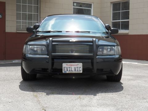 2003 Ford Crown Victoria - Straight-on view of black sedan showing twin spotlights, billet grille, push bar and California EVIL VIC plate.