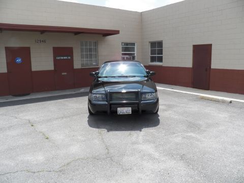 2003 Ford Crown Victoria - Black sedan with push bar photographed head-on in an empty lot beside a beige industrial building.