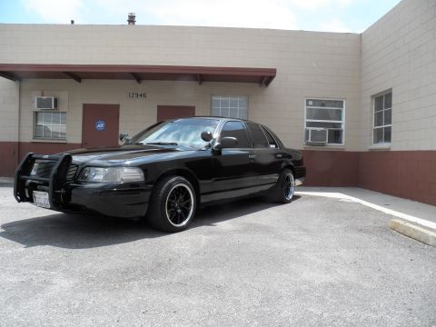 2003 Ford Crown Victoria - Black four-door sedan with front push bar and spotlight parked at the 12946 Custom Mfg Co building.