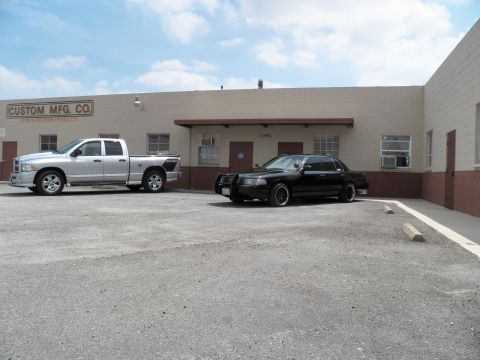 2003 Ford Crown Victoria - Wide view of a silver Ram pickup and a black sedan parked along a beige industrial building.