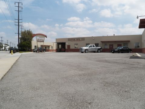 2003 Ford Crown Victoria - Wide gravel lot view of Custom Mfg Co building with a silver Ram pickup and black sedan in the distance.