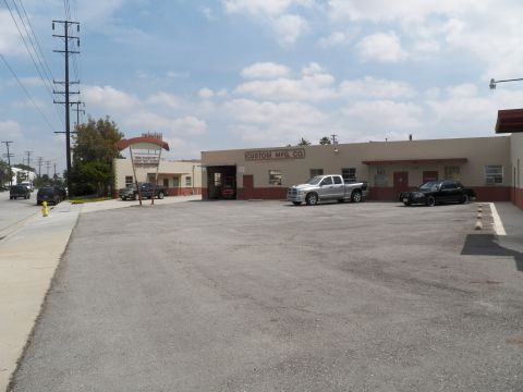 2003 Ford Crown Victoria - Daytime view of the Custom Mfg Co building and gravel lot holding a silver Ram pickup and a black sedan.