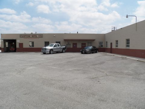 2003 Ford Crown Victoria - Industrial parking lot view: a silver Dodge Ram crew cab beside a dark sedan at Custom Mfg Co.