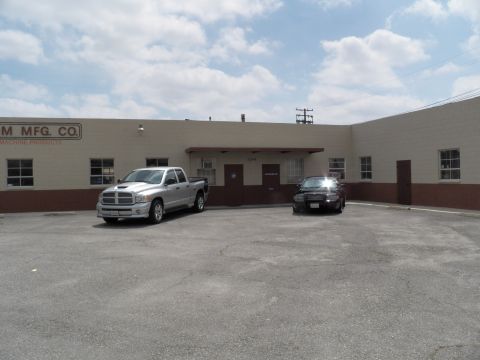2003 Ford Crown Victoria - Two vehicles sit at a tan masonry industrial building marked Custom Mfg Co Machine Products.