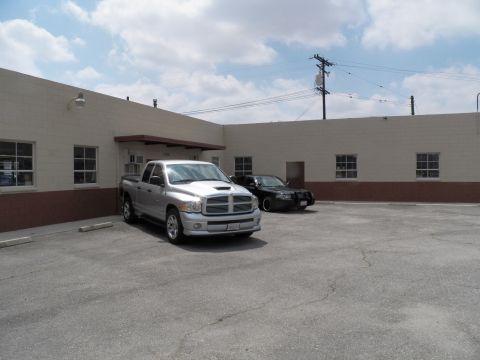 2003 Ford Crown Victoria - silver Dodge Ram crew cab and a dark vehicle in an empty paved lot beside a warehouse.