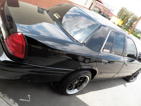 2003 Ford Crown Victoria - Black sedan photographed from a high rear-quarter angle, dark wheels and tinted windows visible.