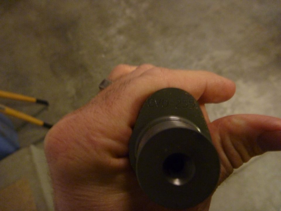 Hand holding a dark cylindrical part with engraved text '20-255'