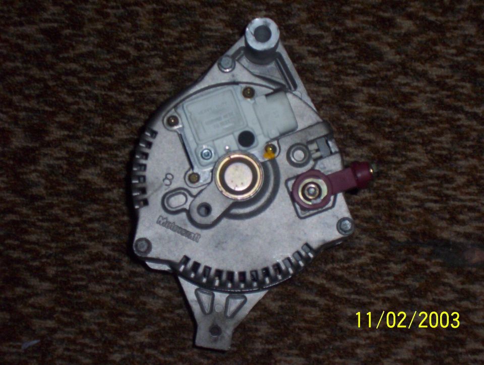 Rear of a Motorcraft alternator with regulator and maroon output terminal, on carpet, dated 11/02/2003