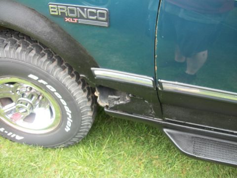 1996 Ford Bronco - Close-up of the side of a 1996 Ford Bronco XLT, showing the fender, tire, and a damaged rocker panel.