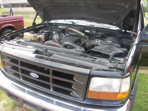 1996 Ford Bronco - Front view of a black Ford truck with its hood open, revealing the engine compartment. A red truck is parked nearby.