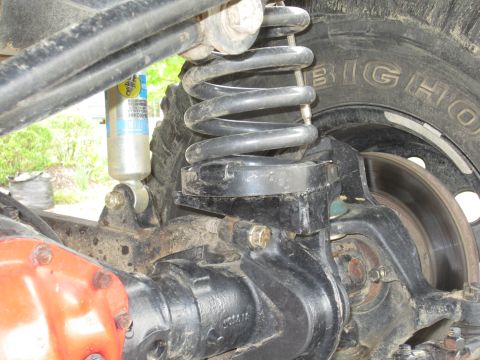 1992 Ford Bronco - Close-up view of the rear suspension system, including a shock absorber and coil spring, with a tire in the background.