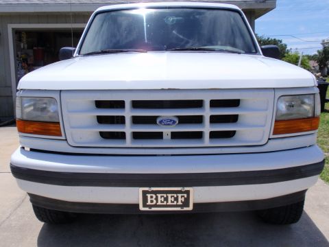 1995 Ford Bronco - Front view of a white Ford truck with a horizontal grille and a custom license plate.