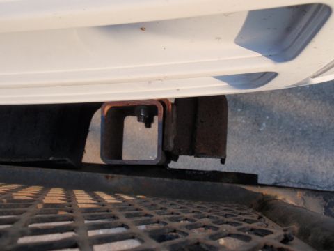 1995 Ford Bronco - Close-up of a trailer hitch receiver on a white vehicle, showing structural components and a metal grate below.