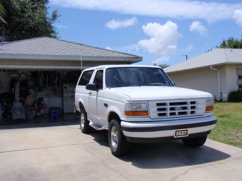 1995 Ford Bronco - A white 1995 Ford Bronco is parked in front of a garage on a sunny day.