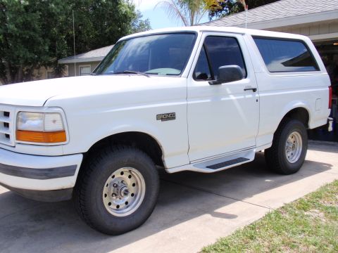 1995 Ford Bronco - A white 1995 Ford Bronco is seen from the front quarter angle, parked in front of a house.