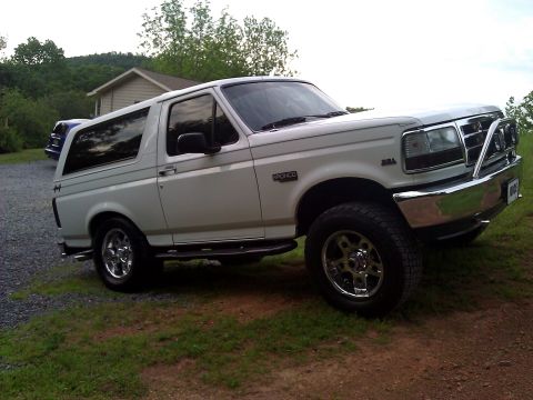 1995 Ford Bronco - This white Ford Bronco is parked on a grassy area next to a gravel driveway, with a house and trees in the background.