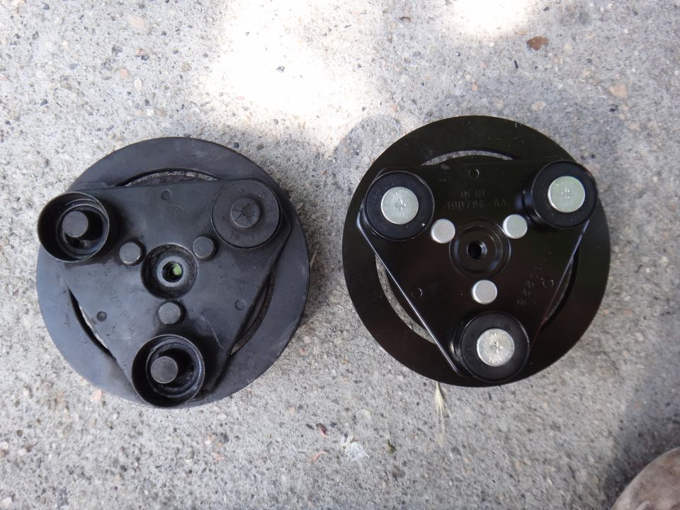 Two black AC compressor clutch hubs shown side-by-side on a concrete surface. One has visible part numbers