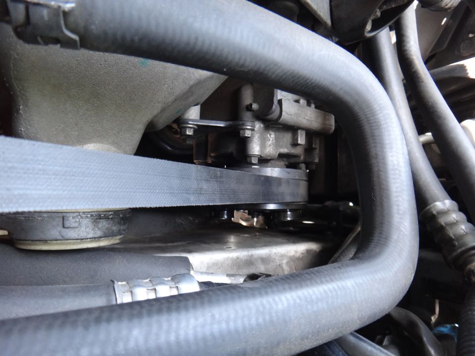 Close-up of a car's engine belt and pulley system, showing the belt tensioner and surrounding hoses