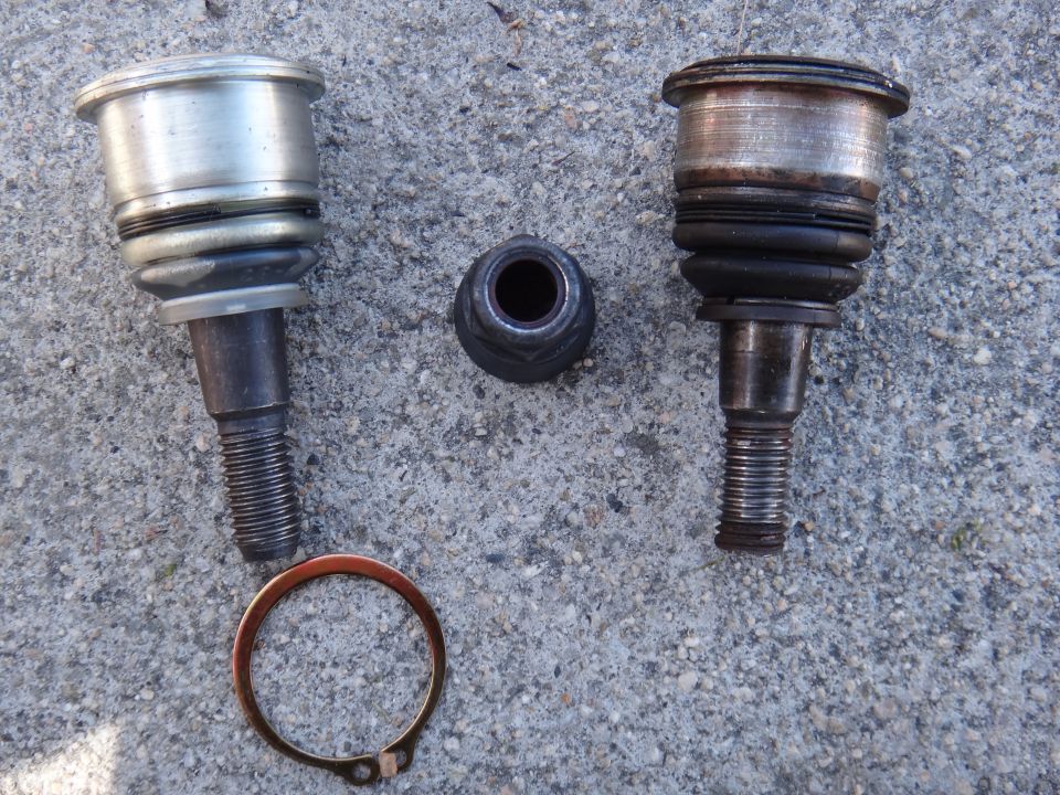 Two ball joints and a nut on a concrete surface. One ball joint is silver and clean, the other is dark and worn