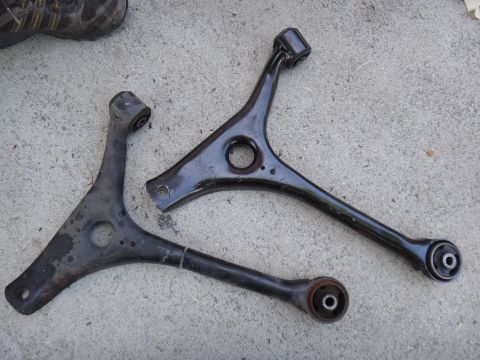 2003 Ford Taurus - Two automotive control arms are shown laid out on a concrete surface.