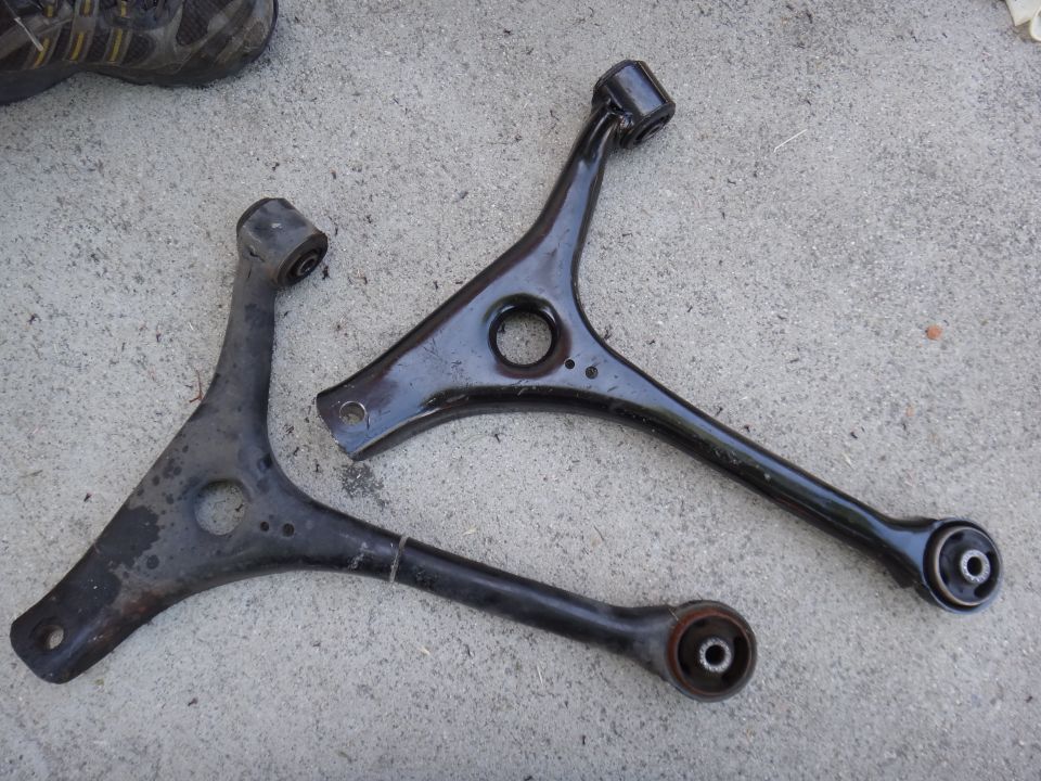 Two black metal control arms with rubber bushings on a concrete surface