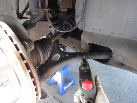 2003 Ford Taurus - A person uses a rotary tool to cut a vehicle's control arm while it's supported by a jack stand.
