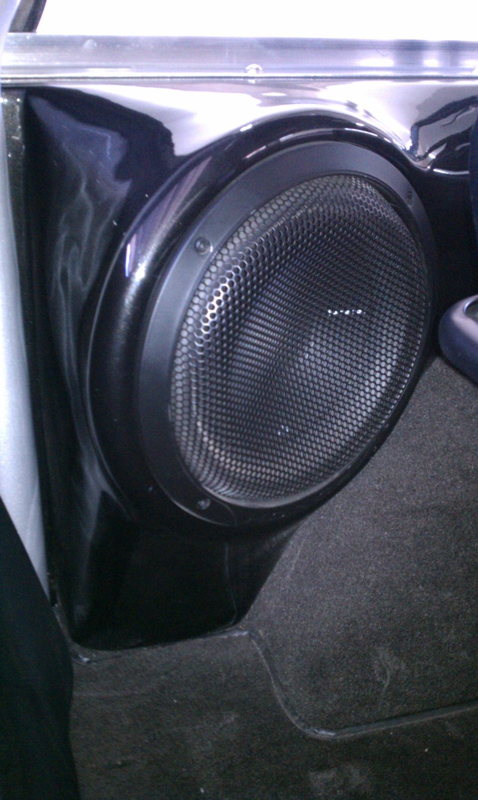 Black subwoofer in glossy custom enclosure inside carpeted vehicle interior