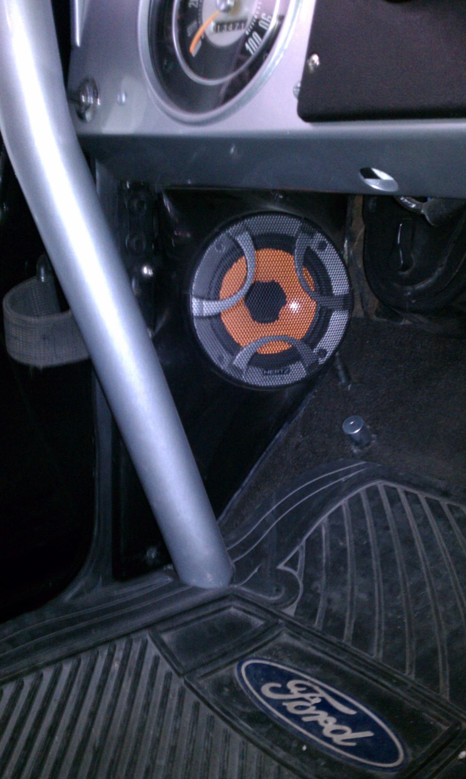 Hertz orange-cone speaker in vehicle kick panel above a Ford logo floor mat
