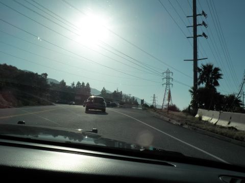 2003 Ford Crown Victoria - Backlit windshield view of an open highway curving past hills, transmission towers at right.
