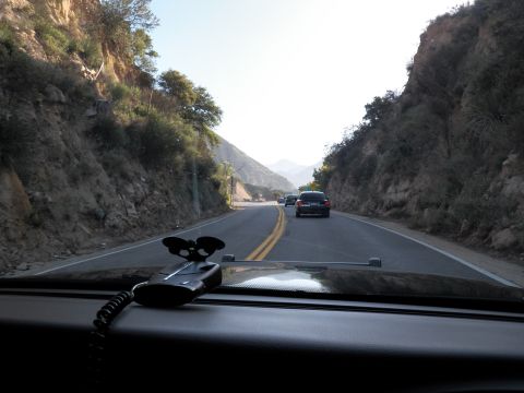2003 Ford Crown Victoria - Two-lane road winds between steep rock cuts; a dark car ahead and dash radio mic in frame.