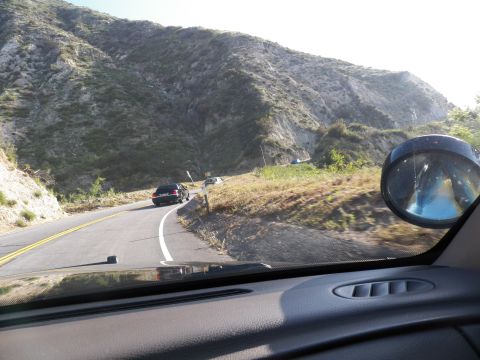 2003 Ford Crown Victoria - Windshield view of a sweeping mountain road bend with a dark sedan ahead and side mirror.