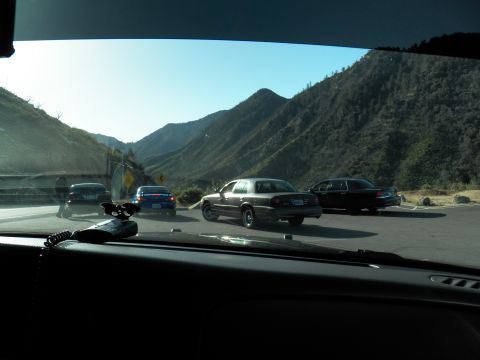 2003 Ford Crown Victoria - Windshield view of several sedans parked at a mountain pullout, jagged peaks in the distance.