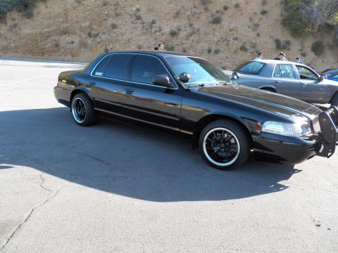 2003 Ford Crown Victoria - Side profile of a blacked-out Ford Crown Victoria with front push bar at a hillside pullout.