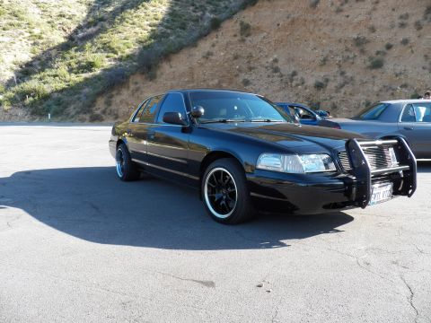 2003 Ford Crown Victoria - Front three-quarter of a black Crown Victoria sporting a brush guard among parked cars.