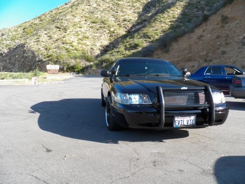 2003 Ford Crown Victoria - Front view of a blacked-out Crown Victoria with brush guard, EVIL VIC plate, hillside behind.